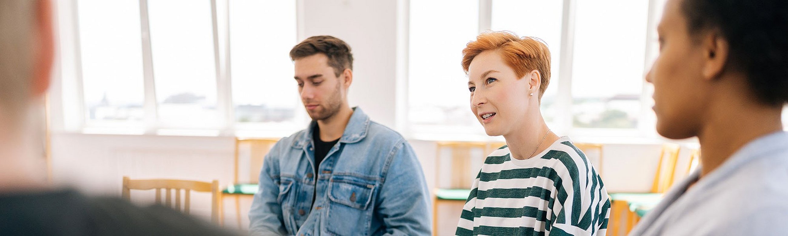 Drei Personen sitzen im Stuhlkreis und hören einer Frau aus der Runde zu.