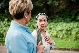 Zwei Frauen unterhalten sich, eine davon trägt eine Kopfbedeckung, weil sie offenbar eine Chemotherapie macht